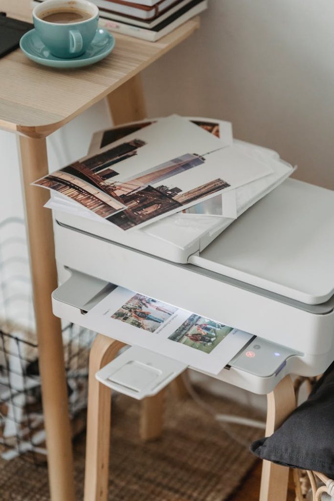 Професионални копирни услуги 14 A cozy home office corner with a printer, coffee cup, and printed photos on a wooden table.